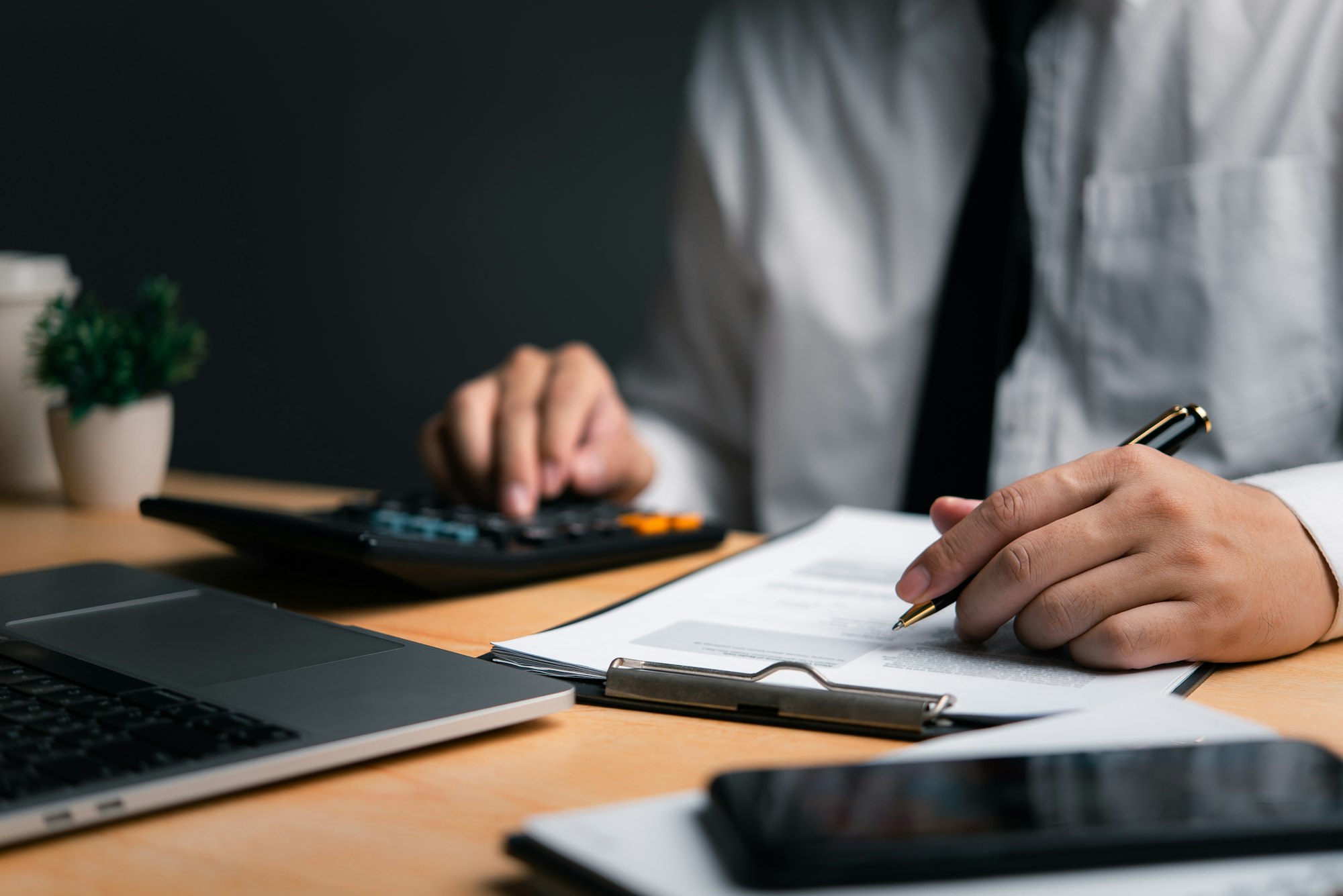 Professional calculating finances on a calculator with documents, laptop and smartphone on desk